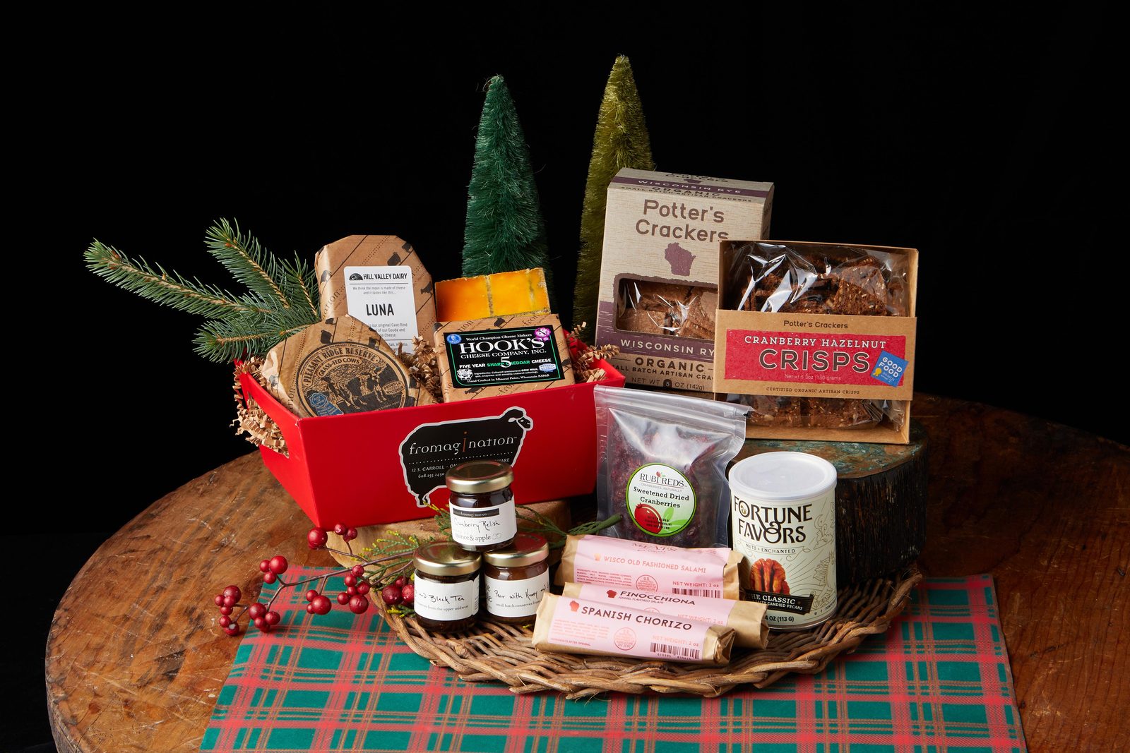 corporate-gifting-award-winning-gift-set-closer A red Fromagination gift box of Wisconsin cheeses, crackers, jams, and sausages on a wooden table.